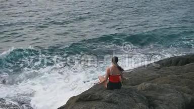 平静的女人在暴风雨的海洋前的岩石海滩上练习瑜伽健身运动